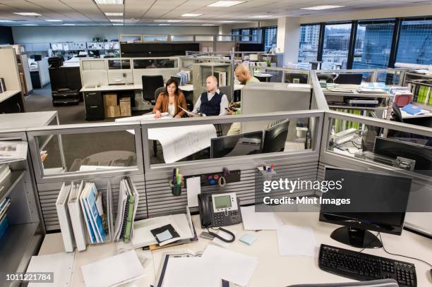wide angle view from above looking down on a mixed race team of three people working on a project in a cubicle office. - office cubicles perspective stock pictures, royalty-free photos & images