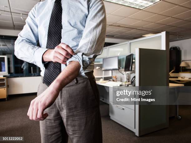 closeup of a caucasian businessman wearing a dress shirt and tie and rolling up his sleeves in his cubicle office. - rolling up sleeve stock-fotos und bilder