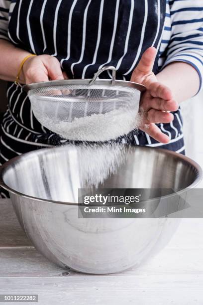 a cook sieving ingredients through a sieve, flour into a metal bowl. - sifting stock photos et images de collection