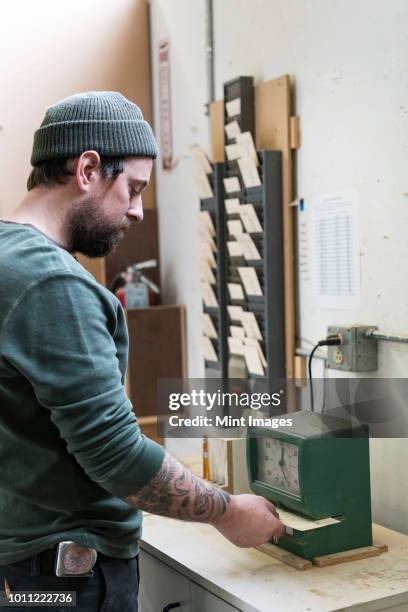 a caucasian carpenter checking in with a time clock in a woodworking factory. - time clock stock pictures, royalty-free photos & images