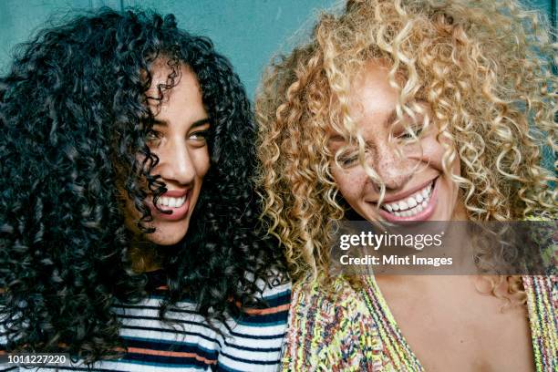 portrait of two young women with long curly black and blond hair, smiling and laughing. - hair curls photos et images de collection