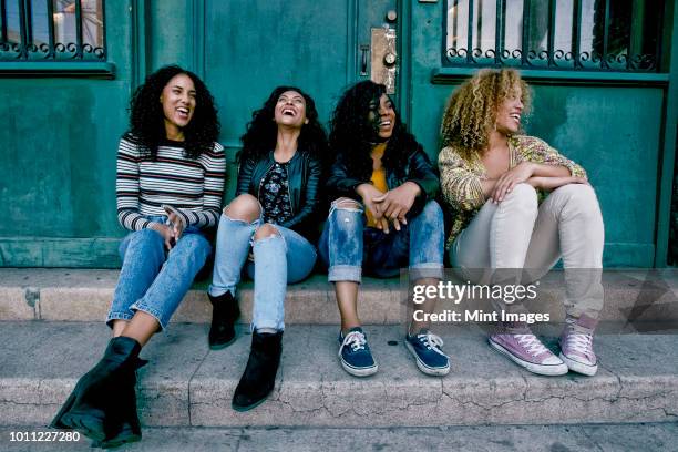 four young women with curly hair sitting side by side on steps outside a building. - 4 steps stock-fotos und bilder