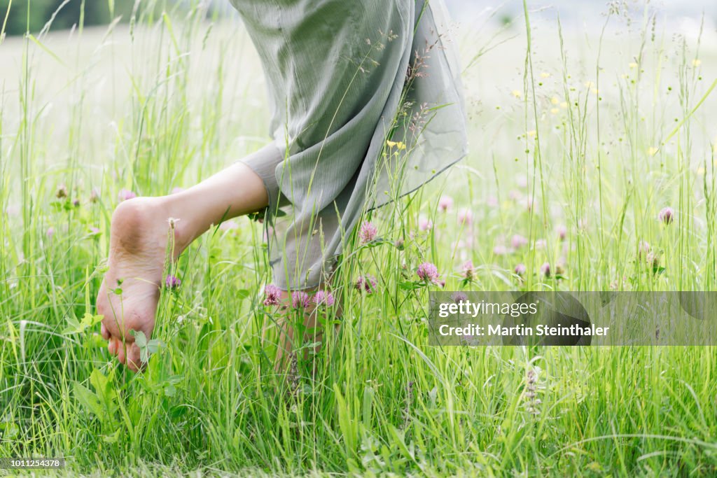 Frau läuft barfuss durch grünes hohes Gras