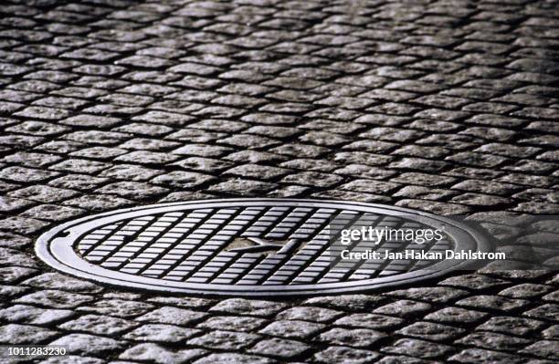 manhole in cobblestone street - canalisation stock-fotos und bilder