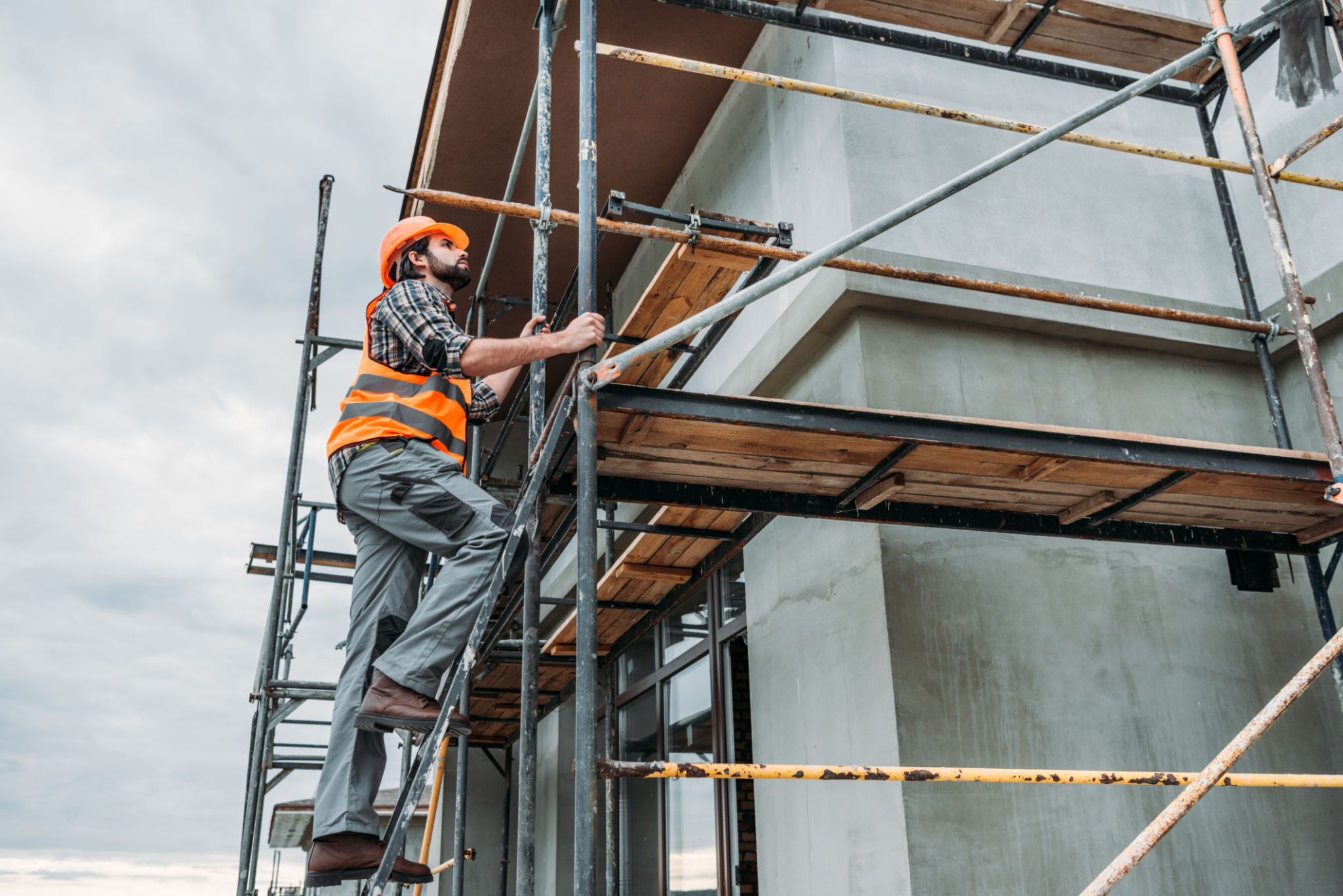 handsome builder climbing on scaffolding at construction site handsome builder climbing on scaffolding at construction site