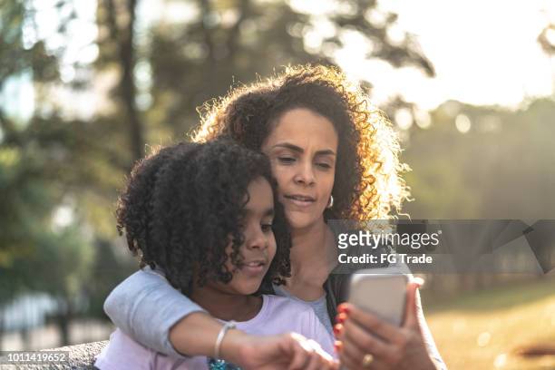daughter and mother using mobile at park - text messaging mother stock pictures, royalty-free photos & images