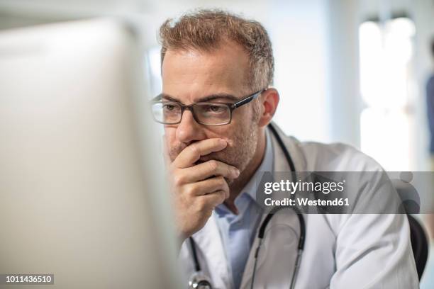 doctor sitting at desk working on computer - worried doctor stock pictures, royalty-free photos & images