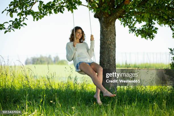 smiling young woman sitting on swing - woman on swing stock-fotos und bilder