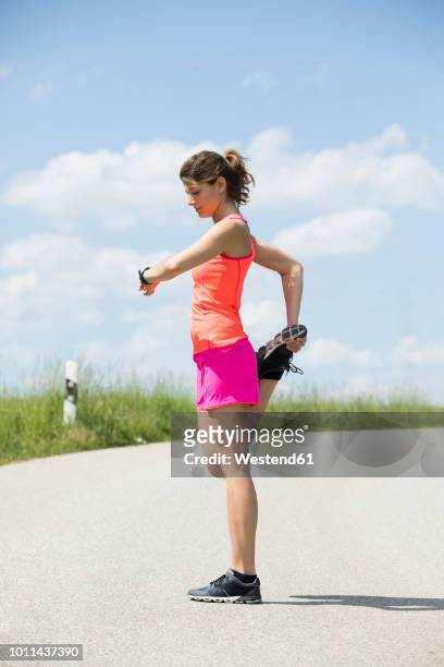 smiling young woman stretching leg and looking on smartwatch - smart watch stock pictures, royalty-free photos & images