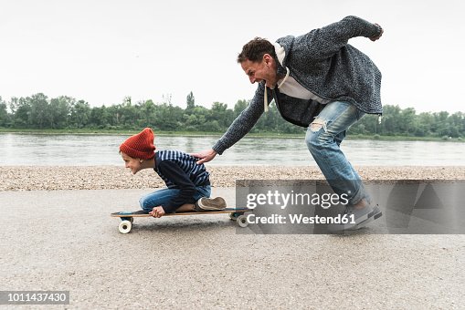 Happy father pushing son on skateboard at the riverside Happy father pushing son on skateboard at the riverside