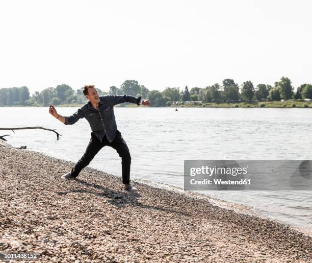 mature man throwing stone at rhine riverbank - flip stock-fotos und bilder