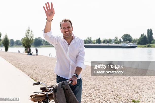 mature man with bike waving at rhine riverbank - hombre alzando los brazos saludando fotografías e imágenes de stock