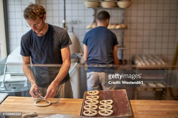 bakers in bakery preparing fresh pretzls - brezel stock-fotos und bilder