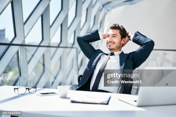 smiling businessman leaning back at desk in modern office - sunny bildbanksfoton och bilder