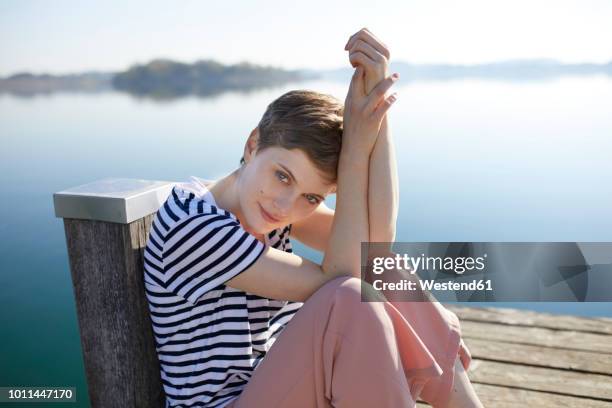 portrait of woman sitting on jetty at lake - woman short hair stock pictures, royalty-free photos & images