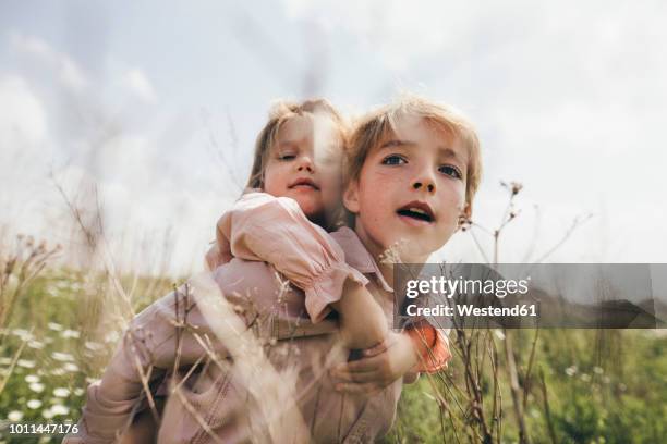 portrait of boy giving his little sister a piggyback ride - sister foto e immagini stock