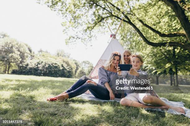 two young women and a boy taking a selfie next to teepee in a park - kampeertent stockfoto's en -beelden