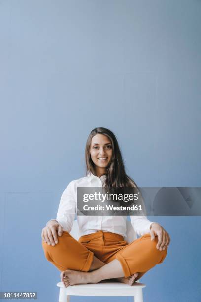 pretty young woman sitting cross legged on a chair - gambe incrociate foto e immagini stock