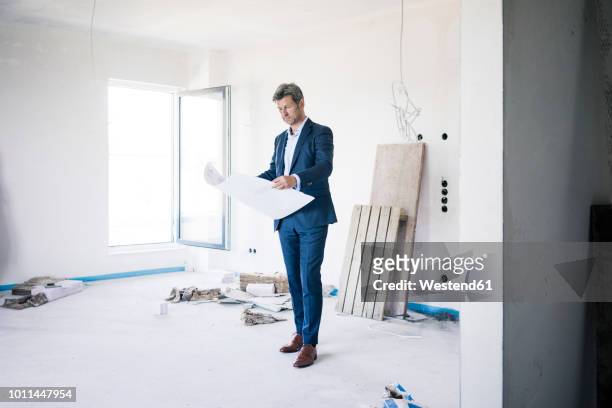 architect holding blueprint in building under construction - person in suit construction stock-fotos und bilder