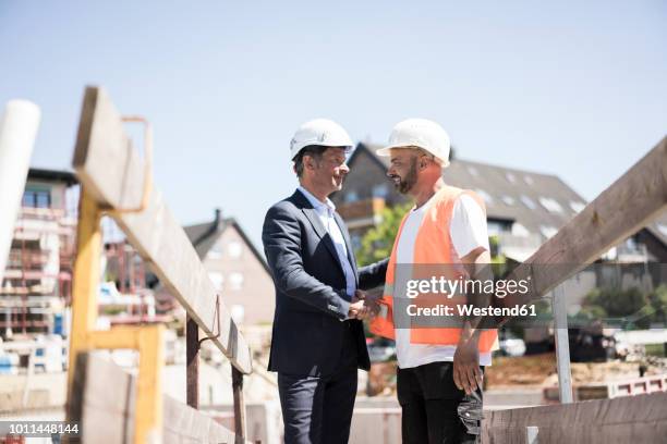 man in suit shaking hands with construction worker on construction site - suit maker stock pictures, royalty-free photos & images