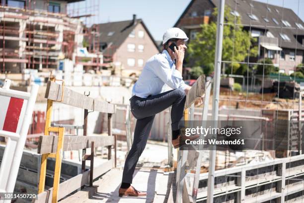 man wearing hard hat on cell phone on construction site - site hoarding stock pictures, royalty-free photos & images