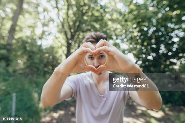 young man making a heart with his fingers on forest path - signaling pathways stock-fotos und bilder