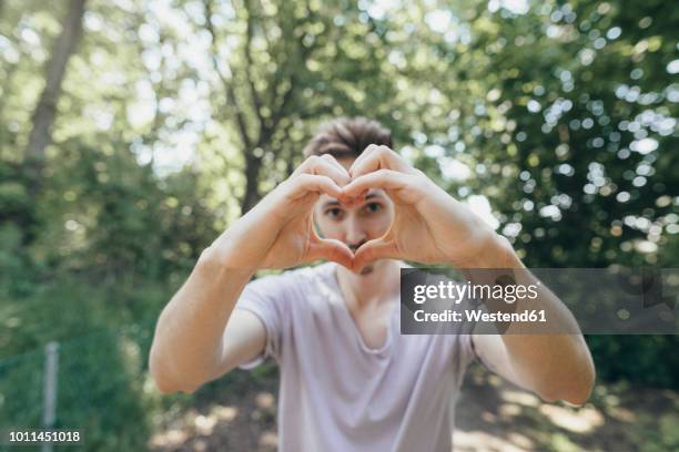 young man making a heart with his fingers on forest path - young at heart ストックフォトと画像