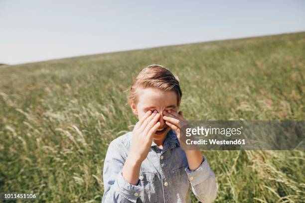 boy on a field rubbing his eyes - allergie foto e immagini stock