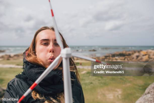 france, brittany, meneham, young woman with miniature wind turbine at the coast - small wind turbine stockfoto's en -beelden