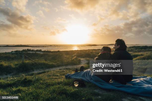 france, brittany, landeda, couple sitting at the coast at sunset - romantische stimmung stock-fotos und bilder