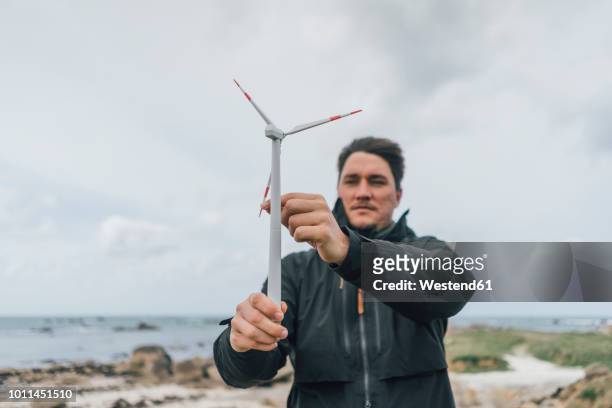 france, brittany, meneham, man with miniature wind turbine at the coast - marine engineering stock pictures, royalty-free photos & images