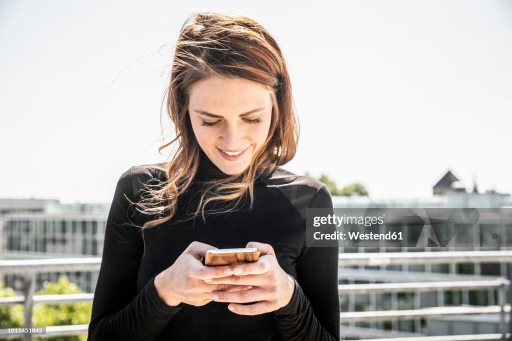 Smiling woman text messaging on roof terrace