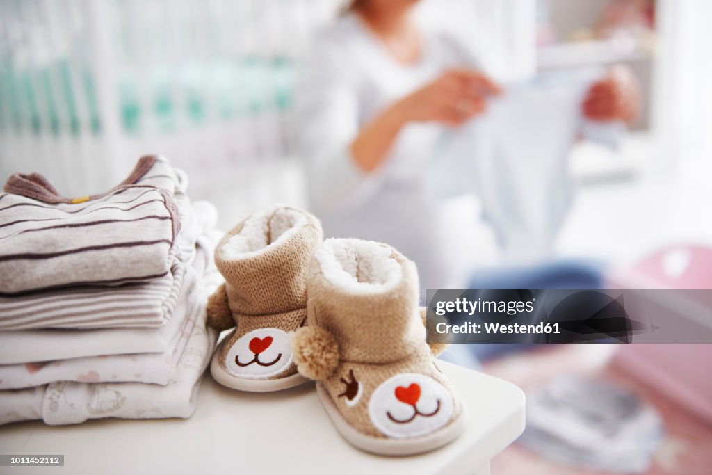Baby shoes and pregnant woman with baby clothes in baby room