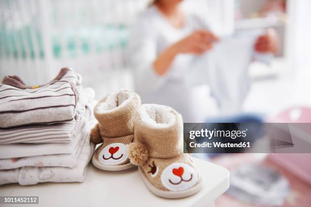 baby shoes and pregnant woman with baby clothes in baby room - babyschuhe stock-fotos und bilder