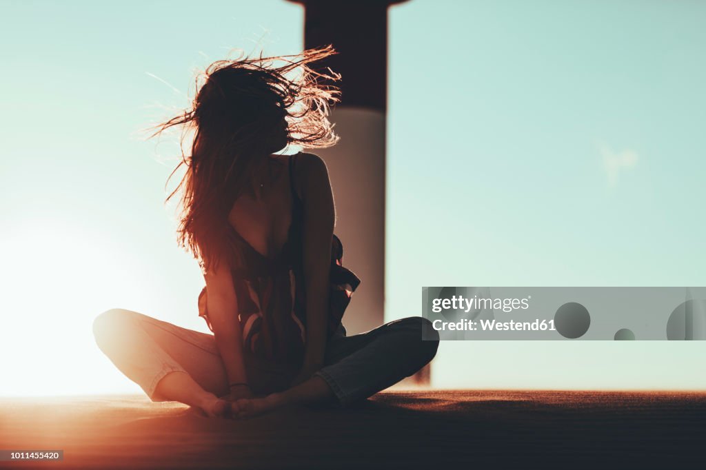 Young woman with windswept hair sitting in desert landscape at sunset