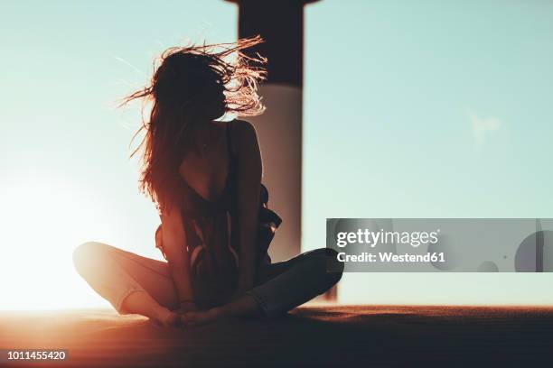 young woman with windswept hair sitting in desert landscape at sunset - solitude desert stock pictures, royalty-free photos & images