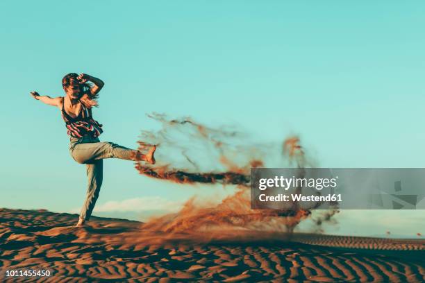 young woman kicking sand in desert landscape - beach dunes foto e immagini stock