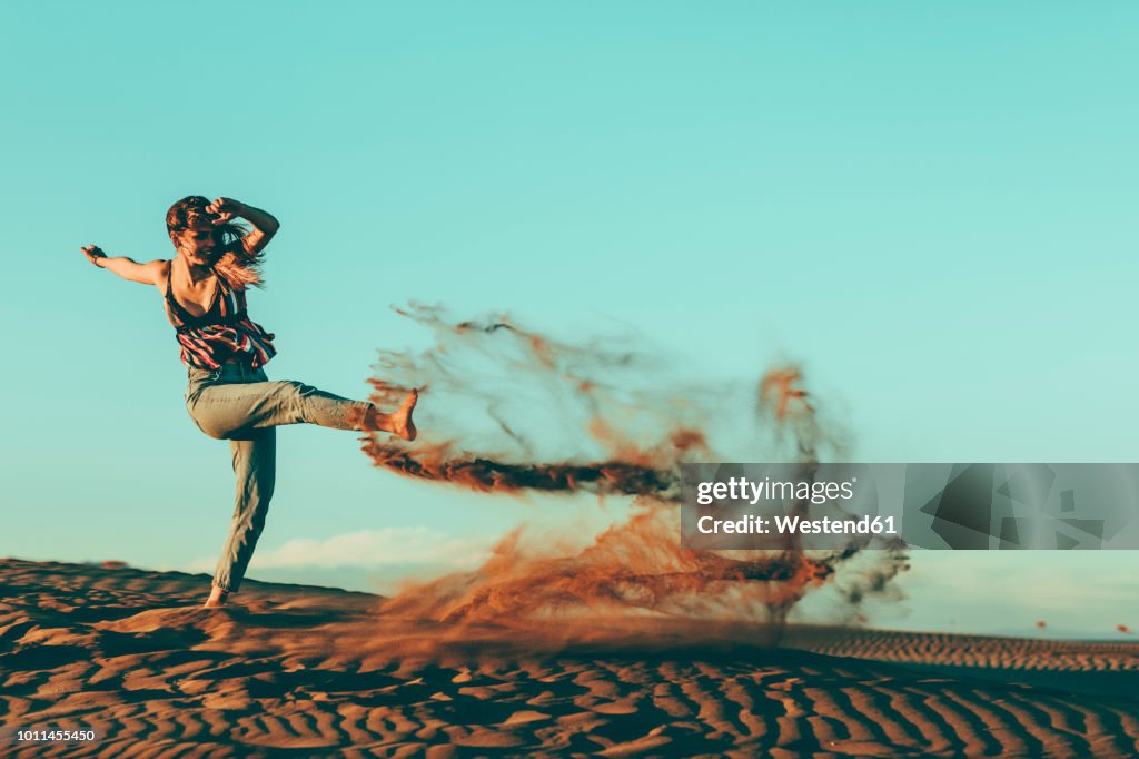 Young woman kicking sand in desert landscape