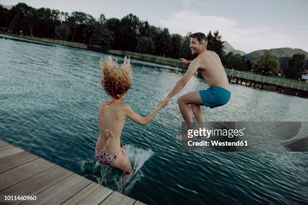 happy couple jumping hand in hand into swimming lake - jumping into lake stock pictures, royalty-free photos & images