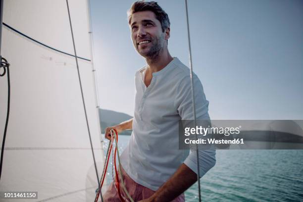 smiling man standing on a sailing boat - segeln stock-fotos und bilder