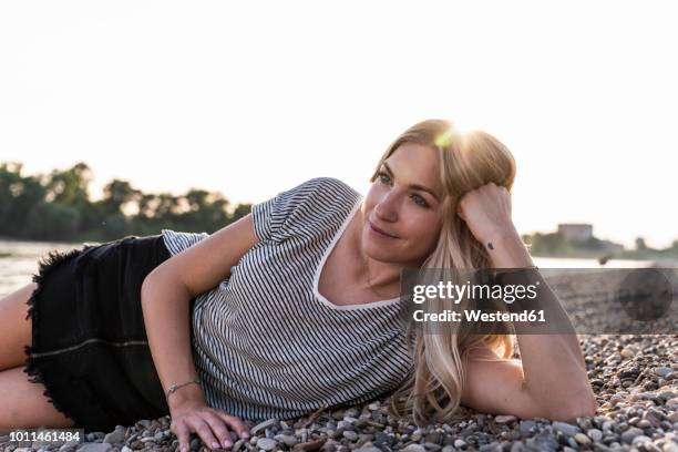 young blond woman lying at riverside against evening sun - acostado de lado fotografías e imágenes de stock