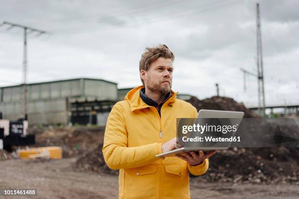 man holding laptop, construction site in the background - construction and engineering stock-fotos und bilder