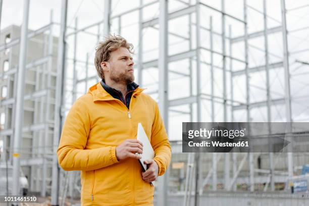 man holding laptop, construction site in the background - architect on site fotografías e imágenes de stock