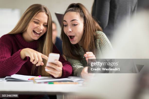 happy teenage girls in class looking at cell phone - toxisch sociaal concept stockfoto's en -beelden