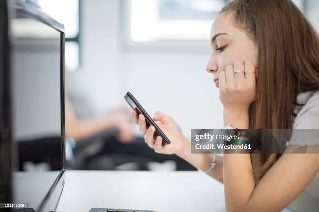 Teenage girl using cell phone in computer class