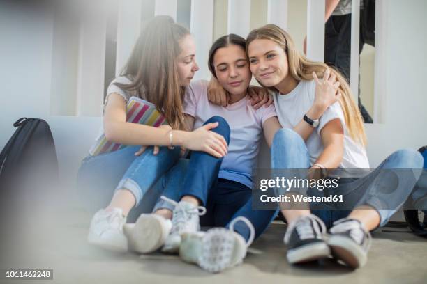 smiling teenage girls sitting on floor in school hugging - consoling teenager stock pictures, royalty-free photos & images