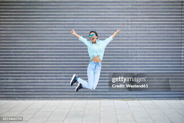 happy woman jumping in the air in front of grey facade - euphorie stock-fotos und bilder