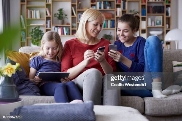 mother and her daughters sitting on couch, having fun using digital laptop and playing with smartphones - family home internet stockfoto's en -beelden