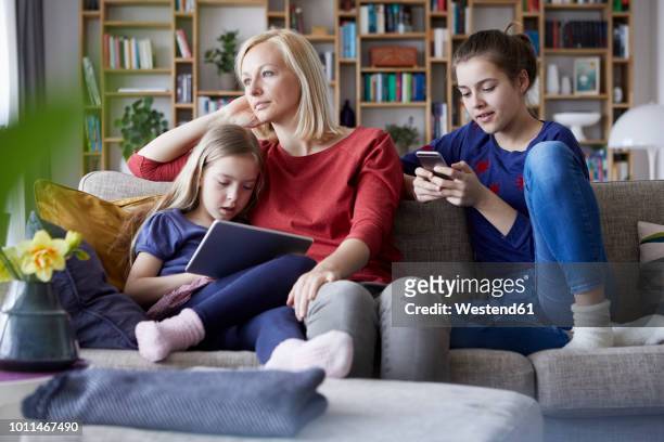 sad mother sitting on couch with her daughters, playing with mobile devices - mobile sad imagens e fotografias de stock