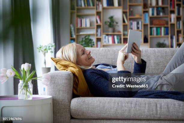 woman using digital tablet, relaxing on couch - woman relaxing tablet fotografías e imágenes de stock